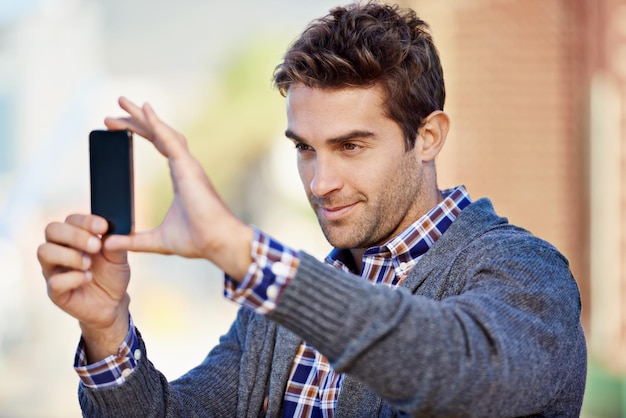 Fotografia por telefone Foto de um jovem bonito tirando uma fotografia com seu telefone celular ao ar livre