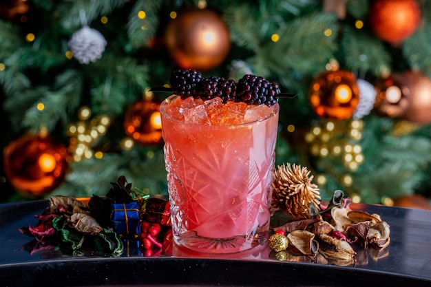 Fotografía en primer plano de un cóctel con bayas en un vaso en el fondo del árbol de Navidad