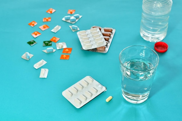 Fotografía en primer plano de diferentes medicamentos, un vaso de agua y una botella de plástico sobre un fondo azul