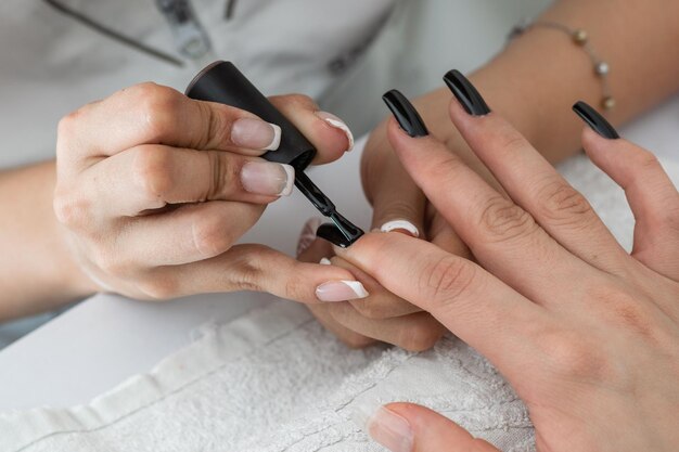 Fotografía en primer plano de una manicurista pintando y diseñando las uñas de una mujer con un esmalte de uñas negro