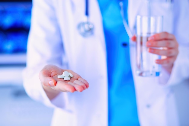 Fotografía en primer plano de las manos del médico sosteniendo pastillas y un vaso de agua