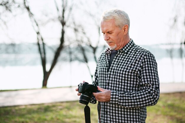 Fotografía real. Hombre senior concentrado mirando hacia abajo y usando la cámara