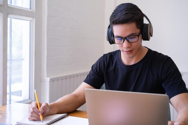 Fotografía recortada de un estudiante universitario asiático usando una computadora portátil y usando auriculares Concepto de tecnología de aprendizaje y ocio