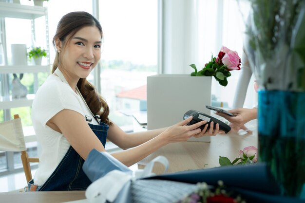 Fotografía recortada de una florista con un teléfono inteligente pagando flores en una floristería