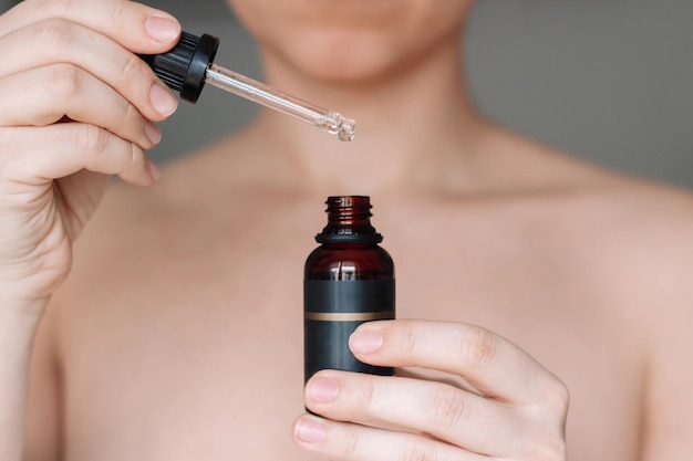 Foto fotografía recortada de una mujer joven sosteniendo un gotero y una botella de vidrio con aceite cosmético esencial