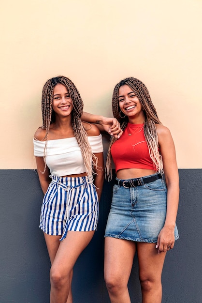 Fotografía de Stock de atractivas hermanas afroamericanas con trenzas frescas sonriendo y mirando a la cámara.