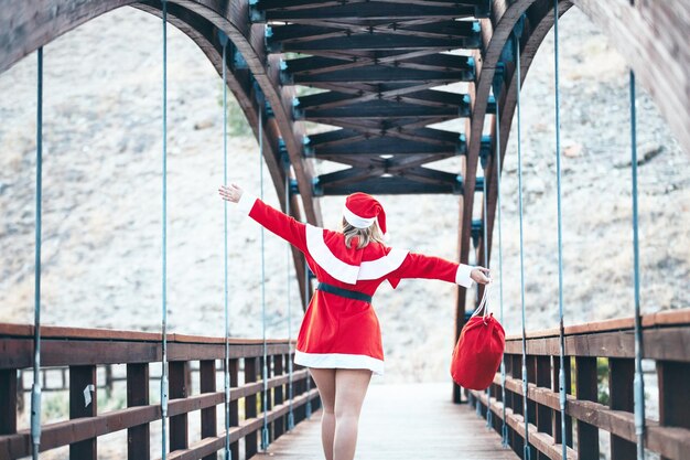 Fotografía de Stock de Mama Noel jugando alegremente con la bolsa roja de regalos en un puente de madera en Navidad