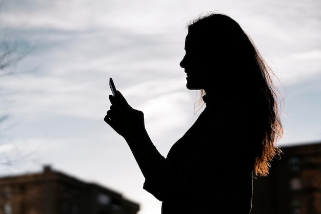 Foto fotografía de stock de una vista lateral de una joven mujer de negocios en las sombras. ella está enviando mensajes de texto.