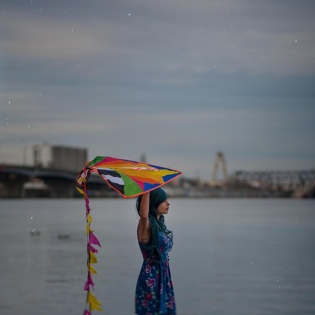 Fotografía surrealista. Retrato de una chica de pelo azul en el paseo marítimo con una cometa en las manos.