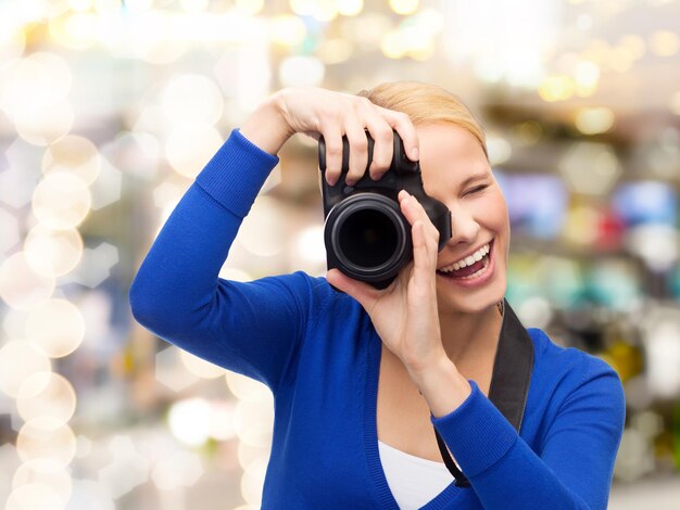 fotografía, tecnología, vacaciones y concepto de personas - mujer joven sonriente tomando fotos con cámara digital sobre fondo de luces