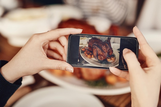 Fotografía telefónica y acción de gracias con las manos de una mujer tomando una foto de la comida en una mesa Redes sociales móviles y Navidad con una mujer usando su teléfono inteligente para fotografiar una comida asada