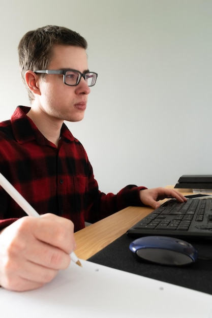 Fotografía vertical de un adolescente caucásico español en una clase en línea con su computadora y tomando notas