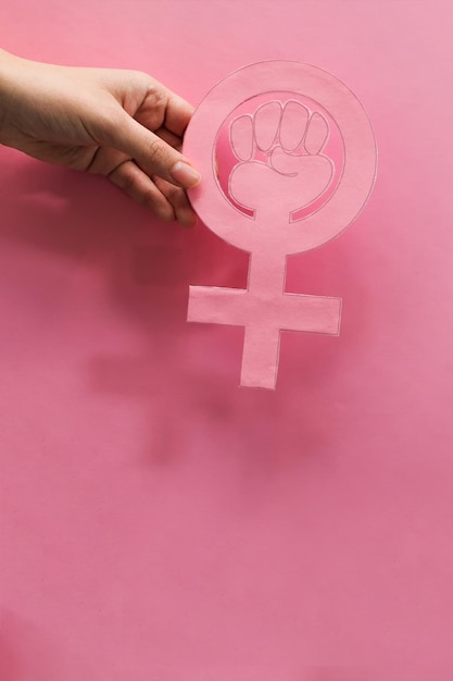 Fotografia vertical de uma mão segurando o símbolo do poder de uma mulher - conceito de feminismo