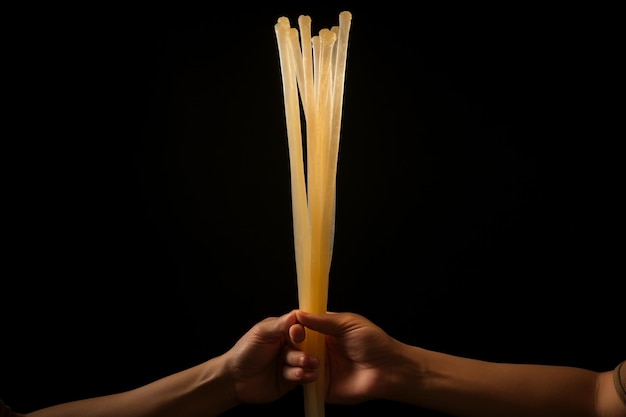 Fotografia vertical de uma pessoa segurando macarrão de vidro cozido com pauzinhos de madeira sob as luzes.