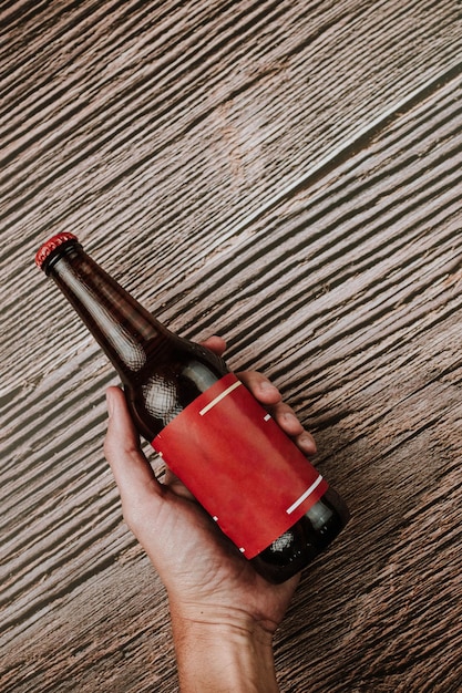 Foto fotografia vertical de uma pessoa segurando uma garrafa de cerveja com um rótulo e tampa vermelhos