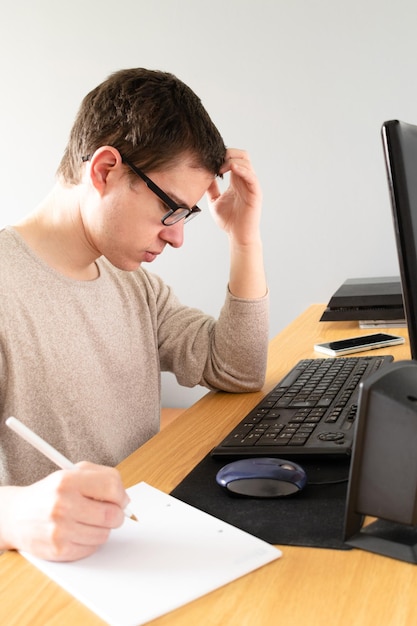 Fotografía vertical de un hombre caucásico español usando su computadora y tomando notas en el interior