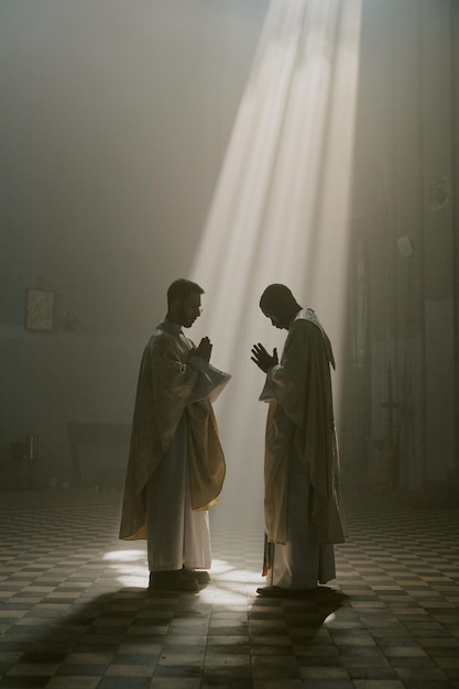 Fotografía vertical de sacerdotes con túnicas blancas con las manos juntas bajo los rayos dorados del sol