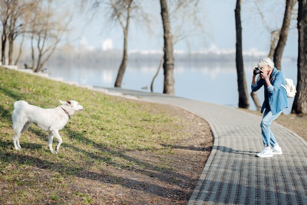 Foto fotografiando. grave mujer madura tomando fotografías de un perro mientras camina en el parque