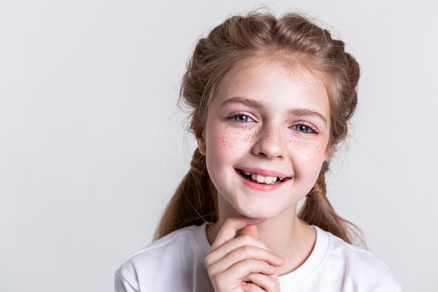 Fotografiar en estudio. Niño bonito contento mostrando sus dientes en amplia sonrisa y tocando la barbilla con los dedos