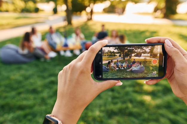 Fotografieren mit dem Smartphone Eine Gruppe junger Leute feiert tagsüber im Sommer eine Party im Park