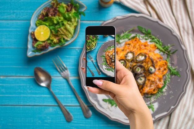 Fotografieren von Food-Konzept-Frau macht ein Bild von Pasta mit Auberginen-Tomaten-Käse-Rucola und Salat