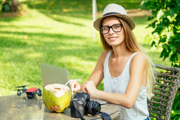 Fotografin, blonde Frau, die im Freien arbeitet und Kokosnuss trinkt