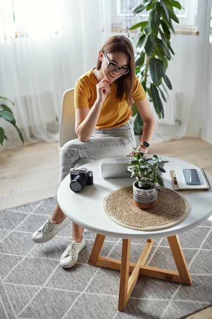 Fotografin der jungen Frau, die zu Hause am Computer arbeitet und zu Hause am Tisch sitzt