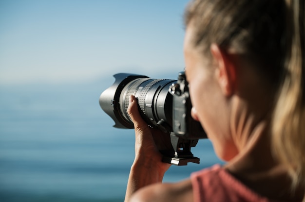 Fotografin, die mit professioneller DSLR-Kamera ein schönes Sommermeer fotografiert.