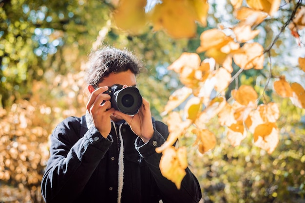 Fotógrafo aficionado masculino disparar hojas de otoño en el parque de la ciudad