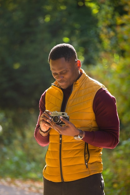 Fotógrafo afroamericano tomando fotos con una cámara vintage en el parque verde de la ciudad, diversidad de actividades de ocio y concepto de hobby