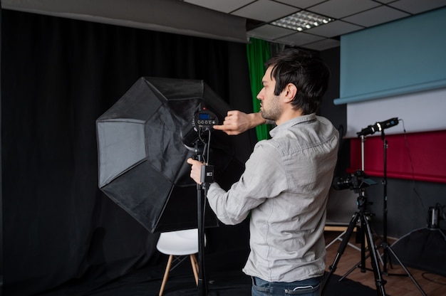 Foto el fotógrafo ajusta la intensidad de la luz de la caja de luz en el estudio. equipo de fotografía de ajuste de hombre preparándose para una sesión de fotos.
