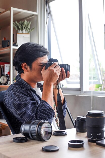 Fotógrafo asiático toma una foto con una cámara dslr sentada en la oficina de producción de fotos y videos