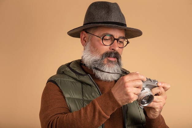 Fotógrafo barbudo con gafas mirando a cámara vintage sobre fondo marrón claro