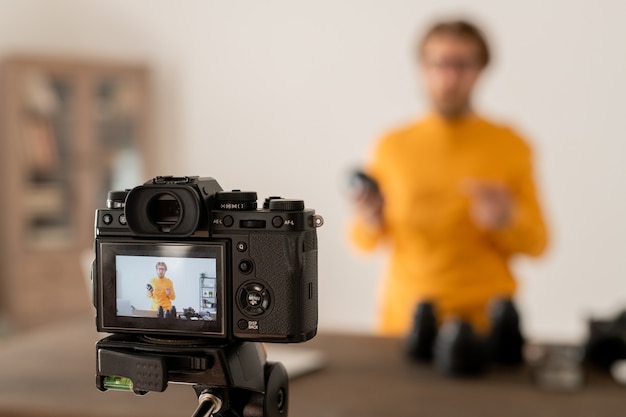 Fotógrafo barbudo que muestra los componentes del nuevo modelo de cámara fotográfica profesional a su audiencia en línea en la lección