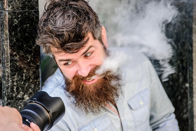 Fotógrafo brutal con cámara. Hipster maduro con barba. Hombre barbudo. equipo fotográfico retro. hombre hipster en gafas de sol de verano. foto de la naturaleza. reportero o periodista. fumando cigarrillos.