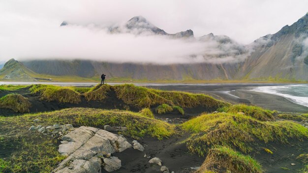 Fotógrafo con cámara y trípode tomando fotos de la montaña Vesturhorn en la mañana de verano. Stokksnes, Islandia. Hermoso paisaje natural escénico. Paisaje de montañas. Atracción turística popular.