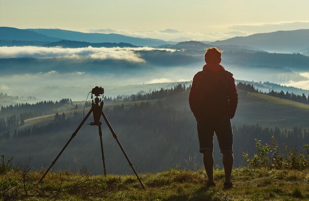 Fotógrafo, câmera tripé e panorama matinal das montanhas dos Cárpatos.