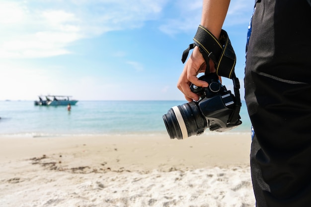 Fotógrafo com viagem da câmera da água do mar e da areia na praia - conceito do curso.