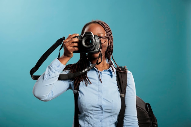 Fotógrafo confiante e criativo tirando fotos enquanto aproveita o tempo de lazer em fundo azul. Entusiasta de fotografia adulto jovem com dispositivo de fotografia moderno tirando fotos. Foto de estúdio