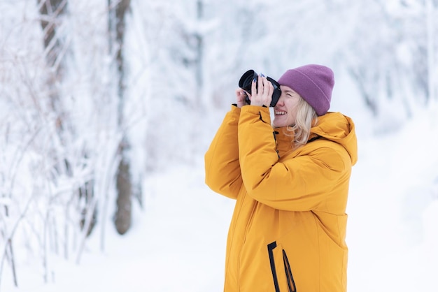 Fotógrafo de garota feliz em uma jaqueta amarela tira fotos do inverno em um parque nevado