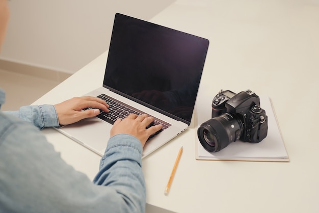 Foto fotógrafo de jovem trabalhando em um computador. mesa de trabalho com teclado, câmera, laptop e lentes.