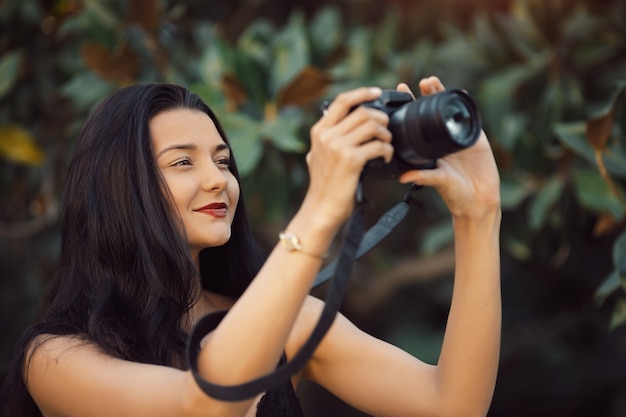 Fotógrafo de mulher atraente tirando fotos com a câmera dslr ao ar livre no parque. Lindo feliz