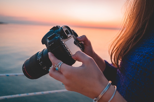 Fotógrafo de mulher detém câmera dslr durante tirar fotos mar ao pôr do sol