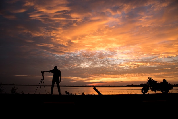 Fotógrafo de silhueta bonito tirar uma foto com a câmera profissional na sunset.