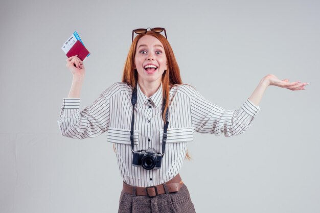 Fotógrafo de turista de empresária feliz ruiva usando óculos escuros estúdio de fundo branco segurando passaporte com visto de ingressos e câmera