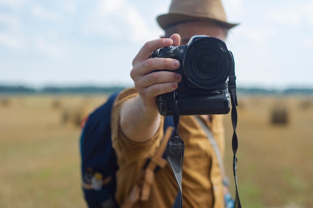 Fotógrafo de viajante com uma câmera na mão no contexto de um campo e montes de feno.