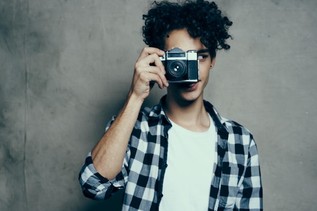 Fotógrafo em uma camisa xadrez com uma câmera na mão em um fundo cinza em uma sala de estúdio de hobby