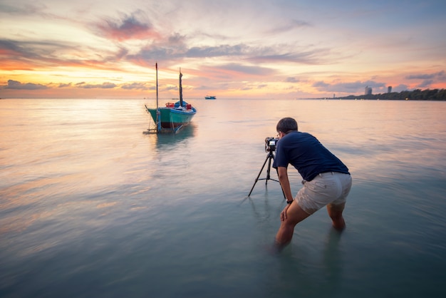 El fotógrafo está tomando una foto del amanecer con barcos de pesca tradicionales