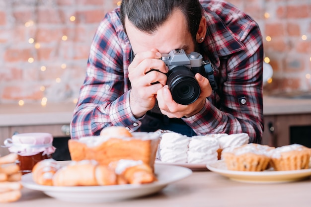 Fotógrafo gastronómico. Surtido de postres. Hombre con cámara tomando fotos de pasteles caseros frescos