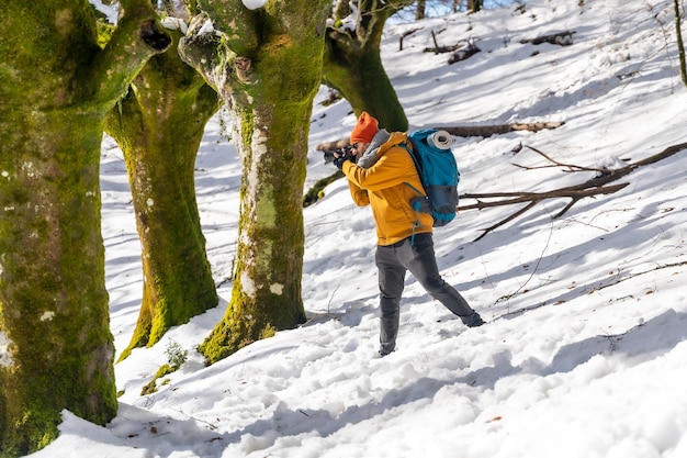 Fotógrafo haciendo un trekking con una mochila tomando fotos de un bosque de hayas con diversión en la nieve y pasatiempos de invierno